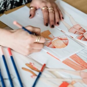 From above of crop unrecognizable female illustrator with pencil coloring sketch of wear on human figure while working on project at desk